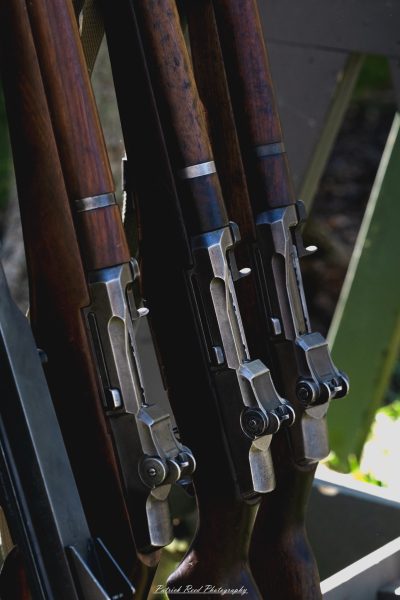 "Close-up shot of M1 Garand rifles arranged neatly, showcasing their distinct features and craftsmanship. The wooden stocks gleam with a rich finish, while the metal parts exhibit wear and patina, reflecting their history. Details such as the barrel, sight, and bolt mechanism are highlighted, emphasizing the rifle's engineering and reliability. The composition captures the essence of this iconic firearm, revered for its role in World War II and its lasting legacy in military history."